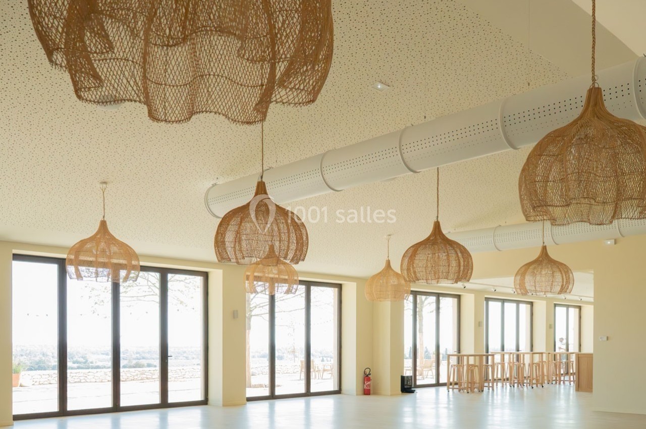 Suspensions en rotin dans une grande salle lumineuse avec baies vitrées donnant sur un paysage extérieur.