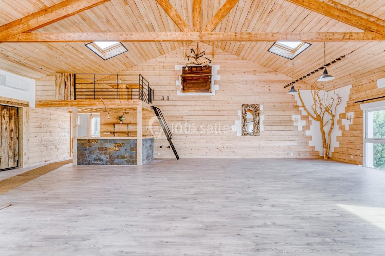 Salle spacieuse en bois clair avec mezzanine, bar en pierre, grandes fenêtres et puits de lumière.