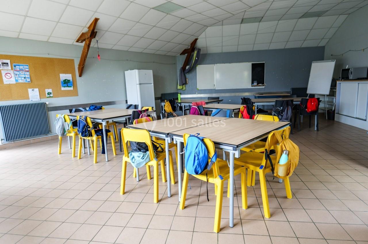 Salle de classe vide avec des tables, des chaises jaunes et des sacs à dos accrochés, tableau blanc en arrière-plan.