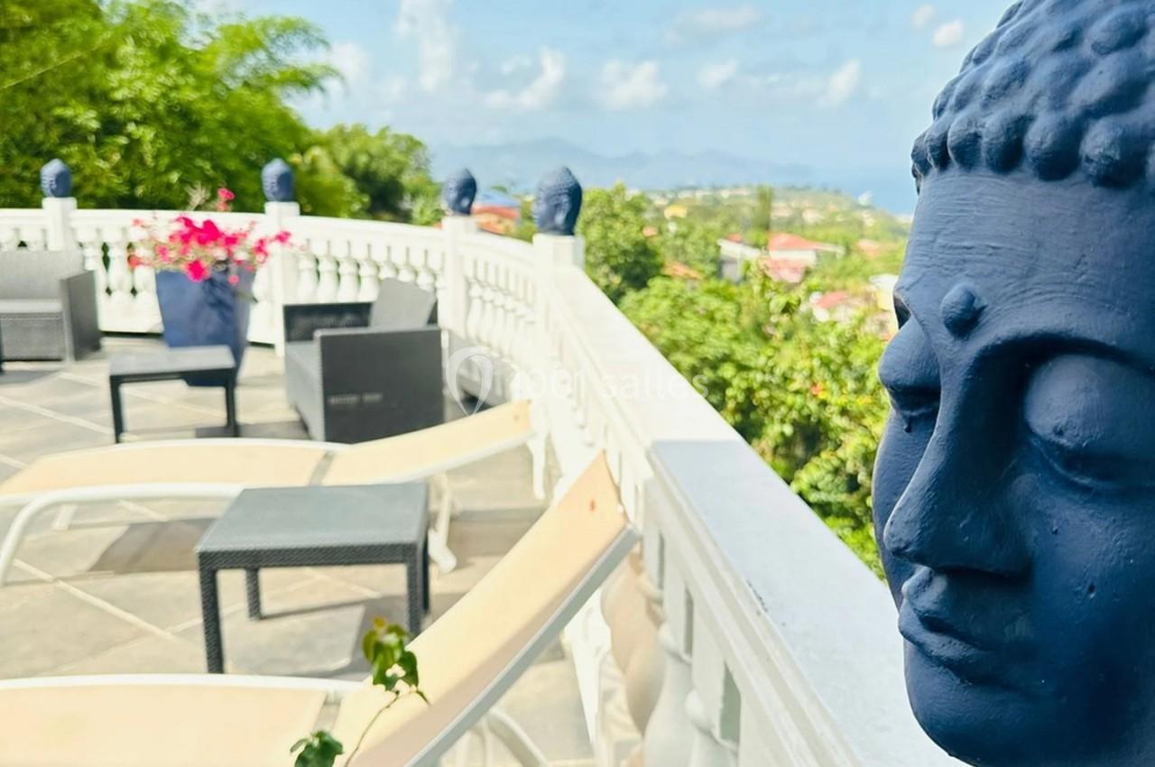 Statues de têtes de Bouddha bleues décorant une terrasse avec des chaises longues et une vue sur la végétation tropicale.