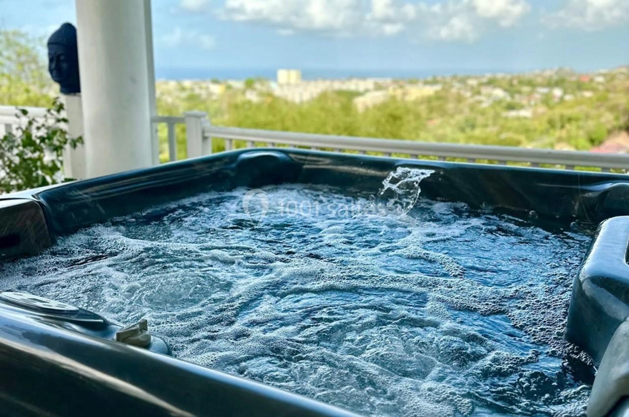 Vue d'un jacuzzi en extérieur avec de l'eau bouillonnante, entouré de verdure et donnant sur un paysage urbain lointain.
