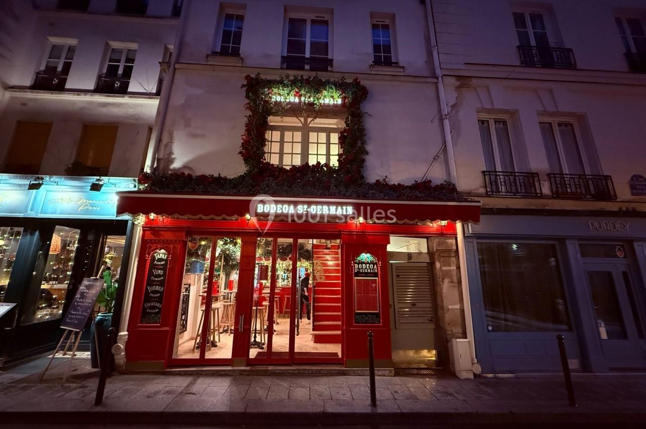 Façade d'un restaurant à l'éclairage rouge vif, avec une entrée ouverte et des décorations florales au-dessus.