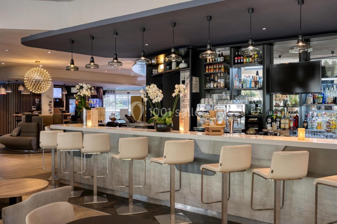 Bar moderne avec comptoir en marbre, tabourets blancs, éclairage suspendu et étagères garnies de bouteilles.