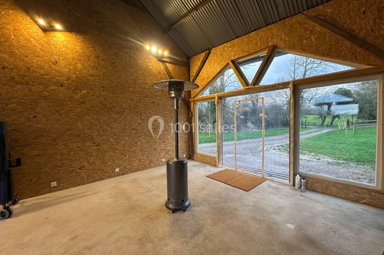 Intérieur d'un bâtiment avec murs en bois, chauffage d'appoint au centre et grande baie vitrée donnant sur un jardin.