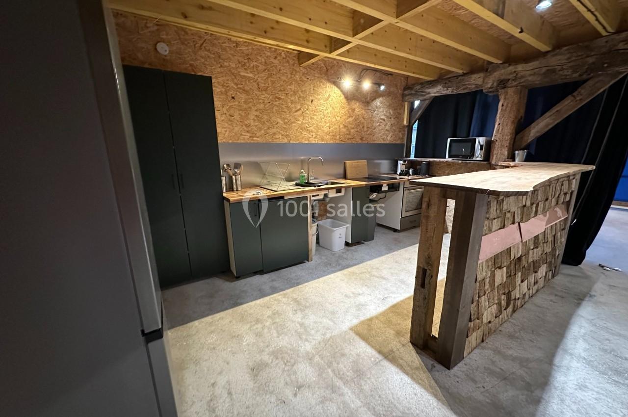 Cuisine ouverte avec plan de travail en bois, armoires vertes, éclairage au plafond et poutres apparentes.