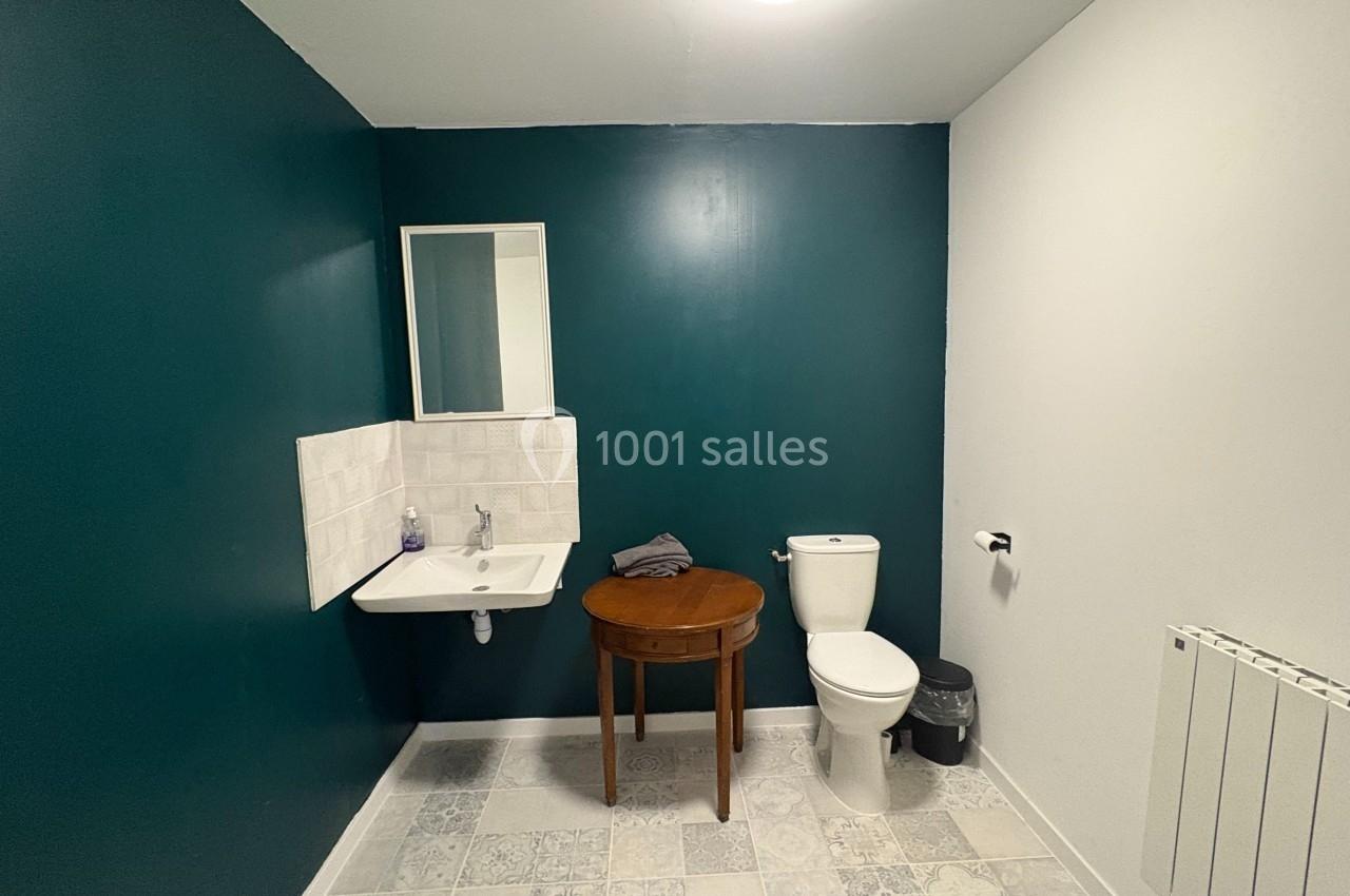 Salle de bain avec mur vert, lavabo, miroir, table en bois, toilettes blanches et sol en carreaux décoratifs.