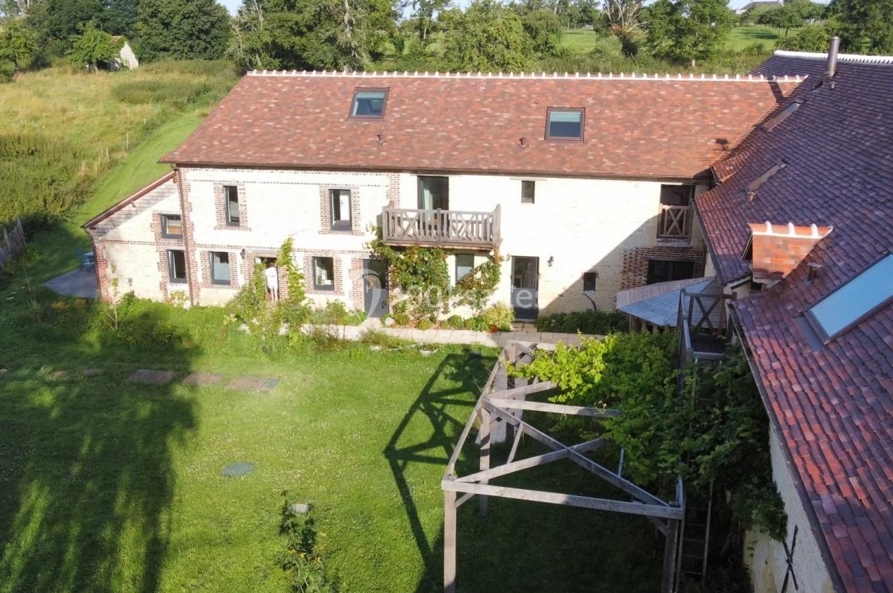 Vue aérienne d'une maison en pierre avec toit en tuiles, entourée d'un jardin verdoyant et d'une pergola en bois.