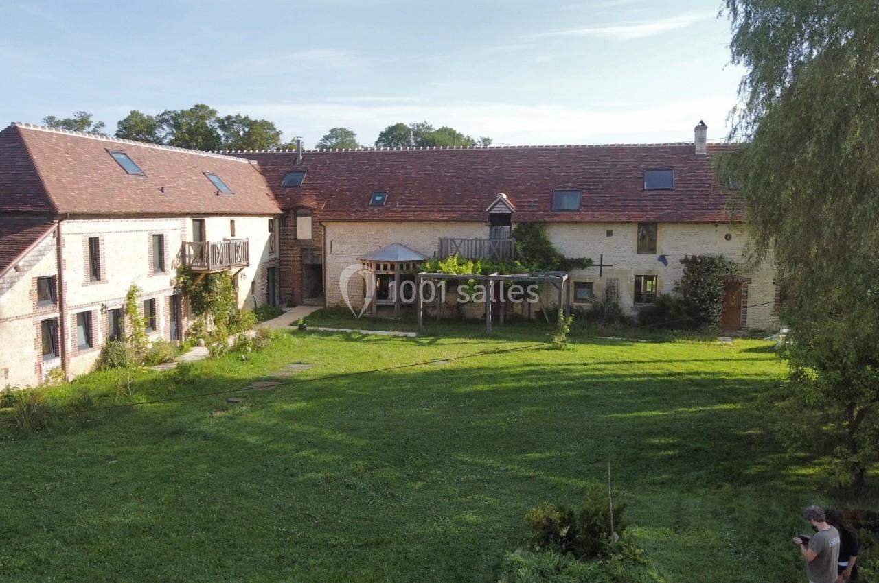 Bâtiment en pierre avec toit en tuiles rouges entouré d'une pelouse et d'arbres sous un ciel dégagé.