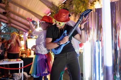 Deux personnes déguisées dansent et jouent avec des accessoires festifs dans un environnement lumineux et animé.