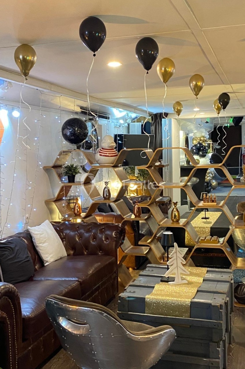 Salon décoré pour une fête avec ballons noirs et dorés, étagères hexagonales et mobilier en cuir et métal.