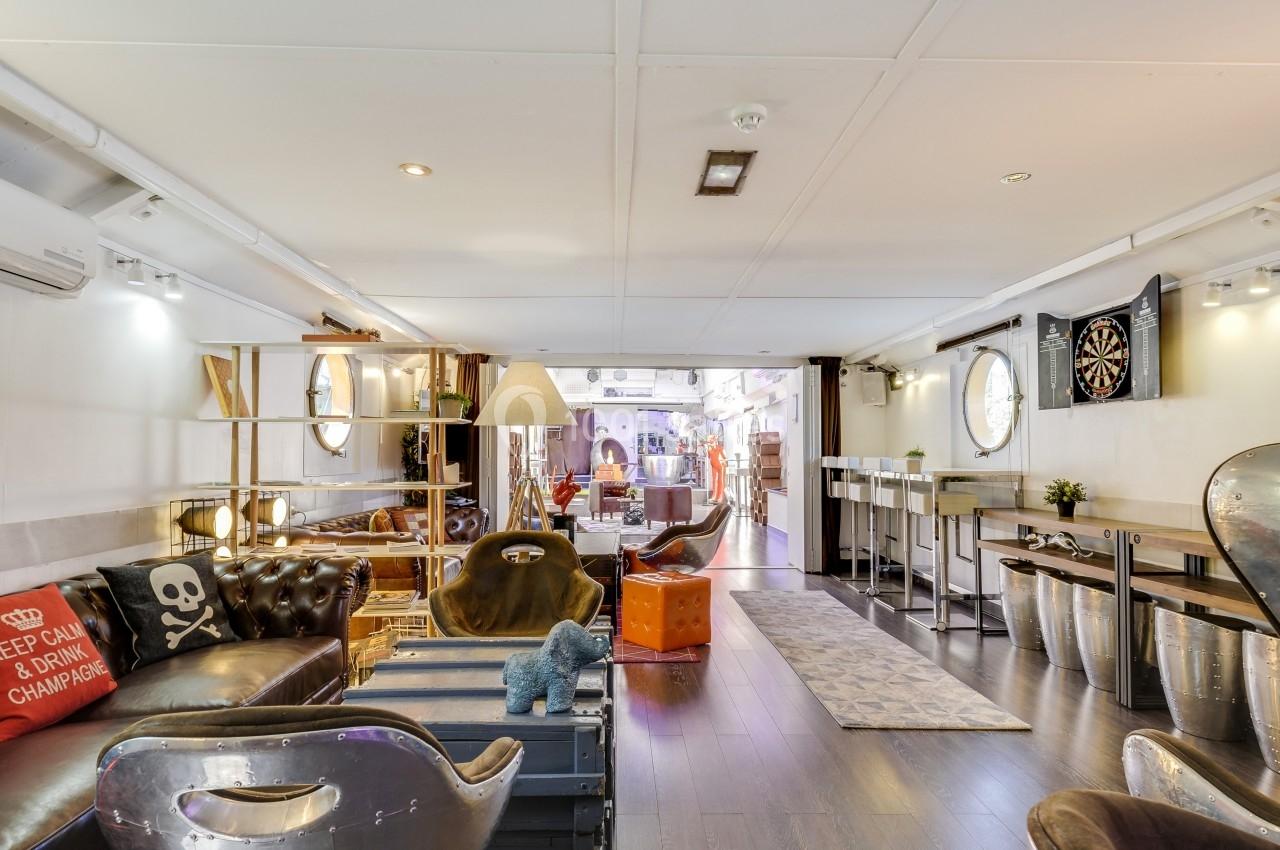 Intérieur lumineux avec mobilier éclectique, fauteuils en cuir, étagères en bois et cible de fléchettes au mur.