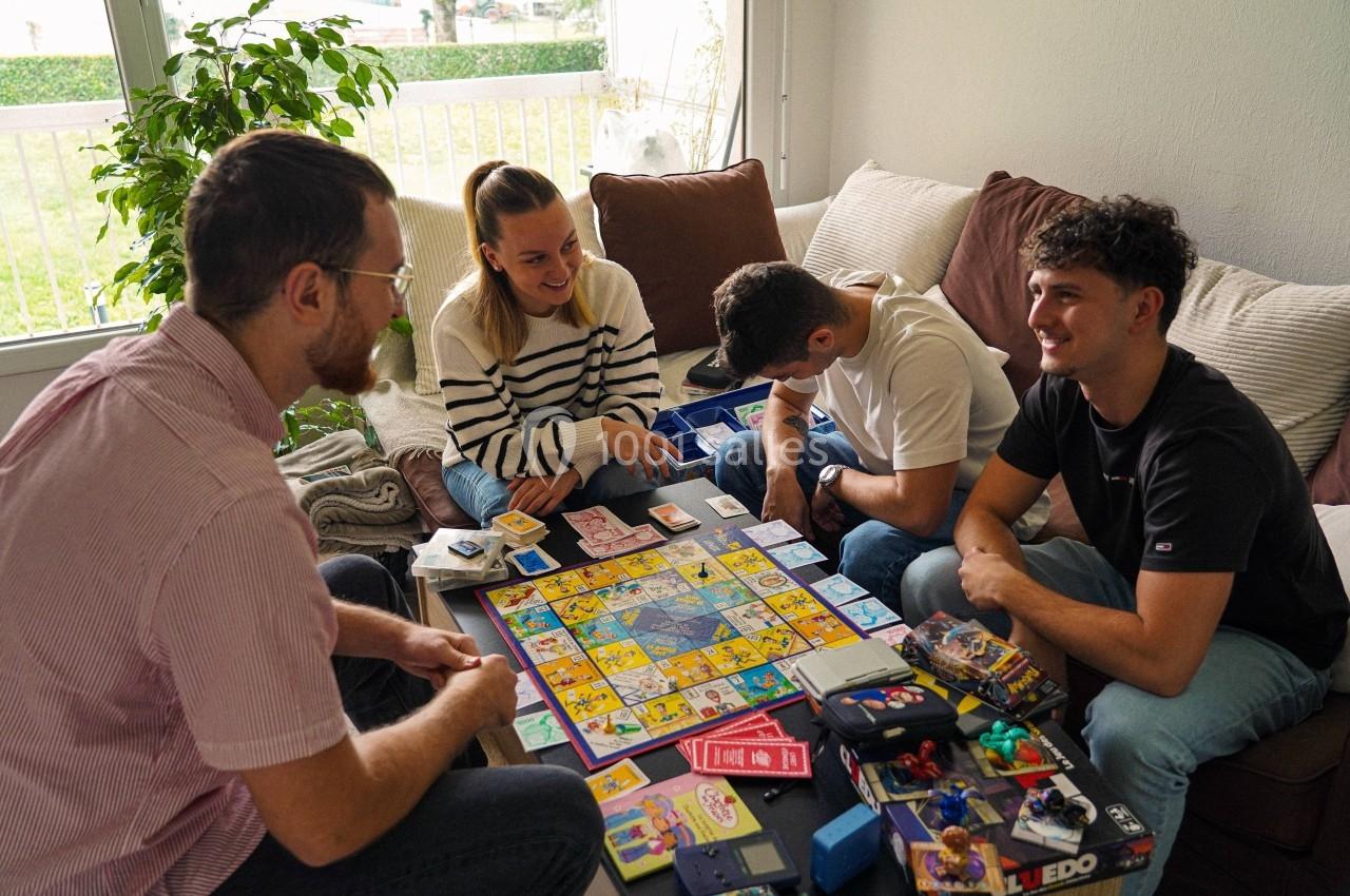 Quatre personnes jouent à un jeu de société autour d'une table basse dans un salon lumineux.