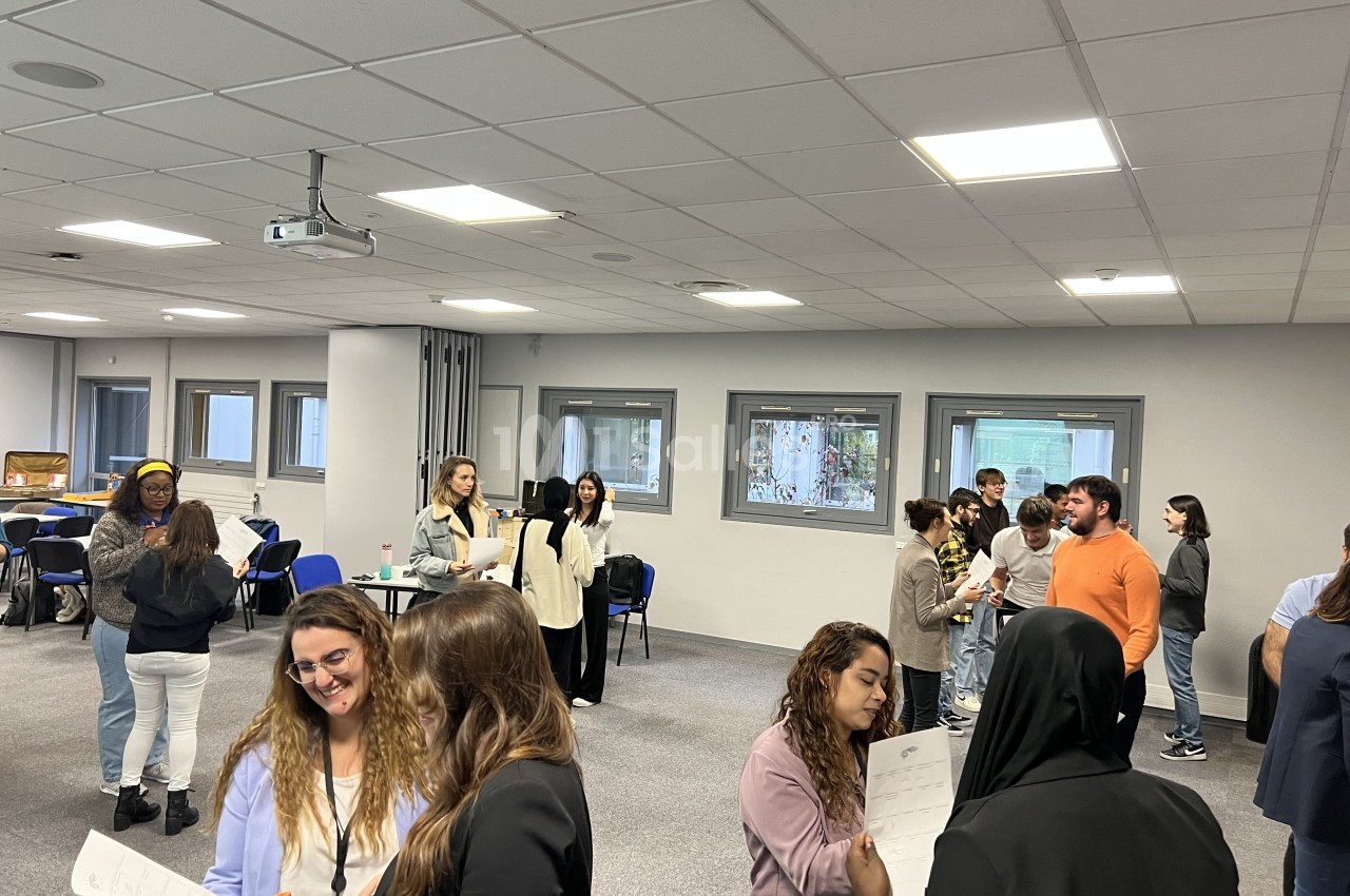 Des personnes discutent en petits groupes dans une salle de réunion lumineuse avec des tables et des chaises en arrière-plan.