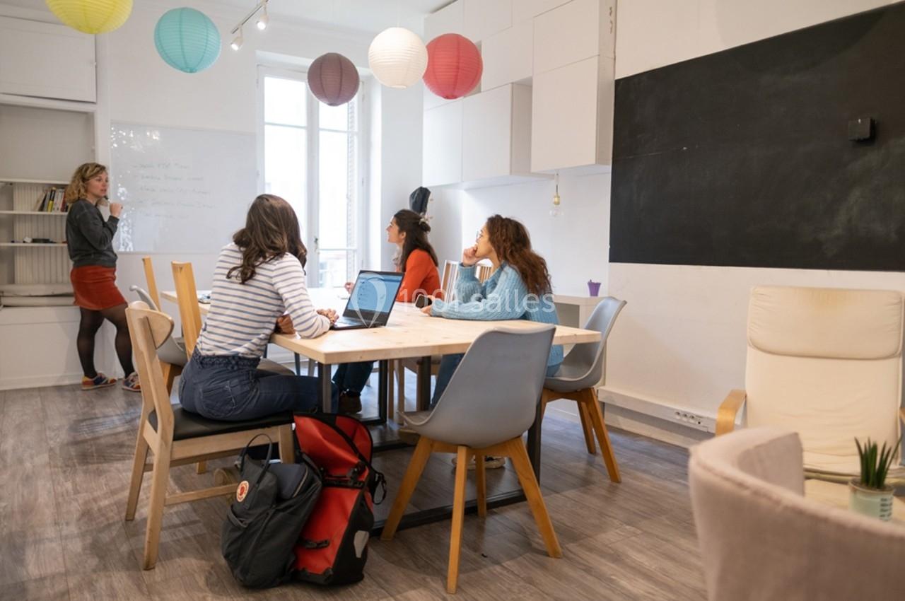 Quatre personnes discutent autour d'une table dans une salle lumineuse, avec une femme écrivant au tableau blanc.