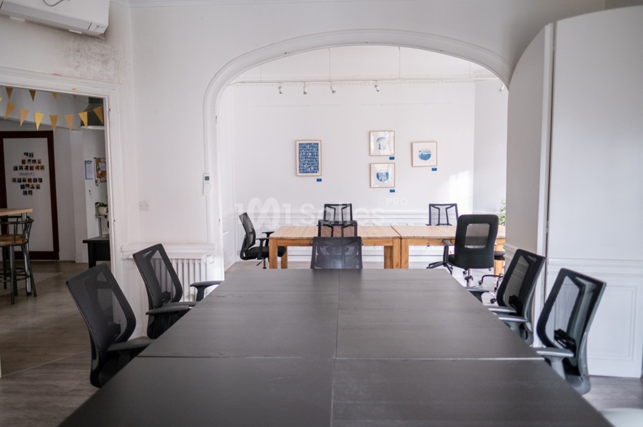 Salle de réunion lumineuse avec une grande table noire, des chaises de bureau et des cadres accrochés au mur.