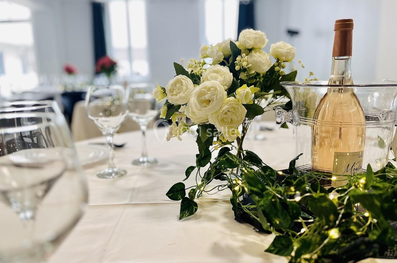 Bouteille de vin rosé dans un seau à glace, entourée de fleurs blanches et de verdure sur une table dressée.