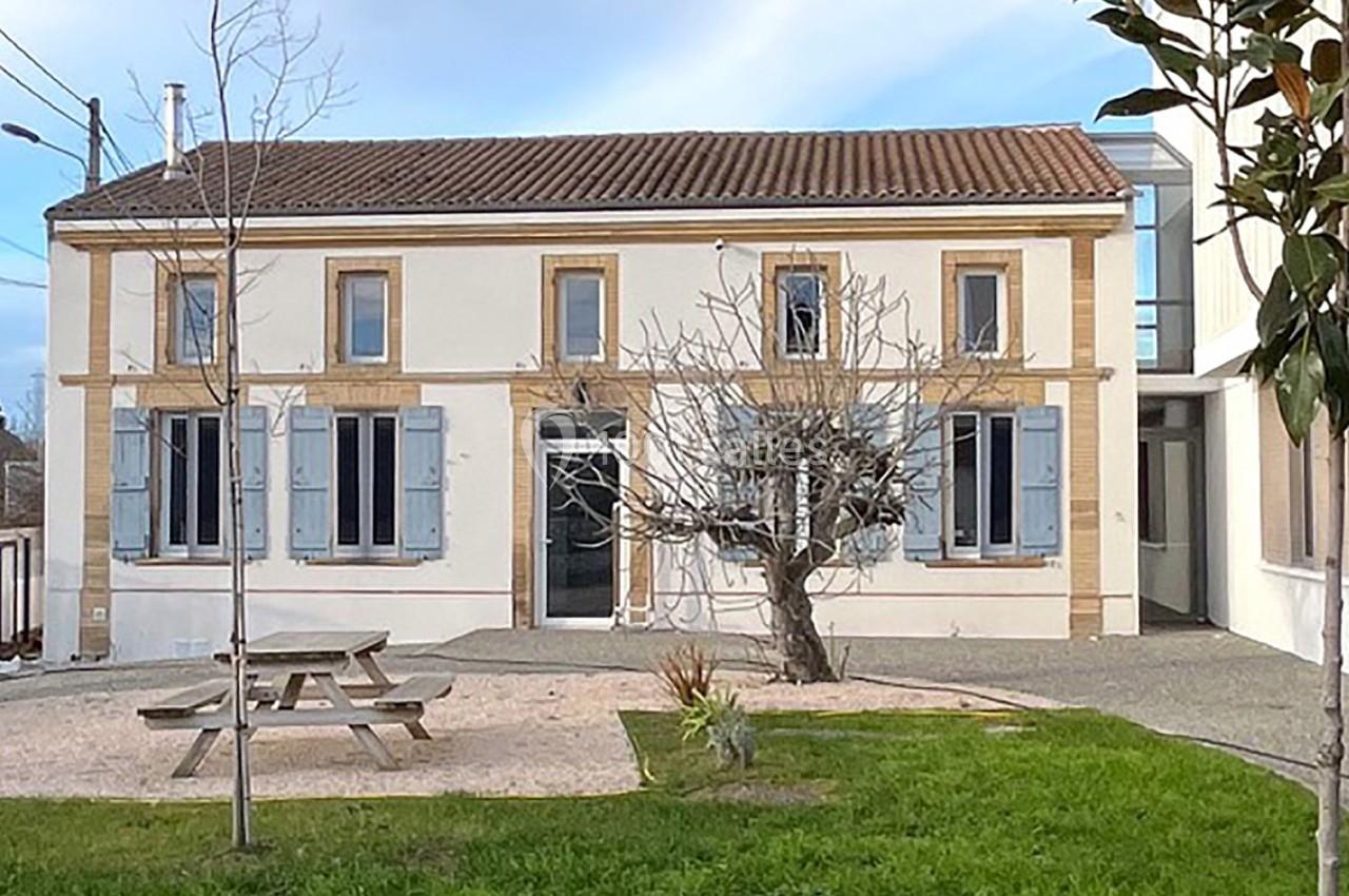 Façade d'une maison à deux étages avec volets bleus, un arbre et une table de pique-nique dans le jardin.