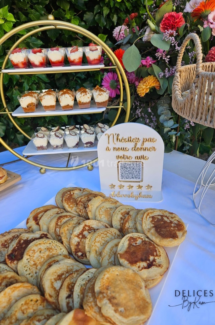 Plateau de pancakes devant un présentoir de desserts variés, décoré de fleurs et d'une pancarte invitant à donner un avis.