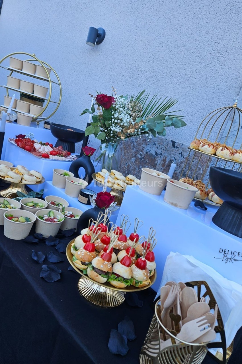Buffet élégant avec verrines, mini-burgers, desserts et décorations florales sur une table extérieure.