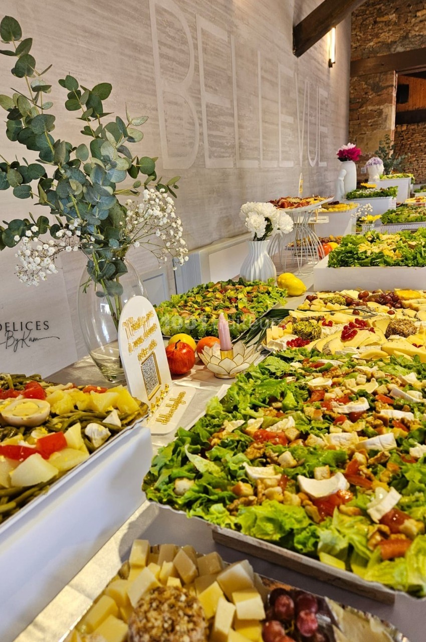 Buffet varié avec salades, fromages, fruits et décorations florales dans une salle lumineuse en pierre apparente.