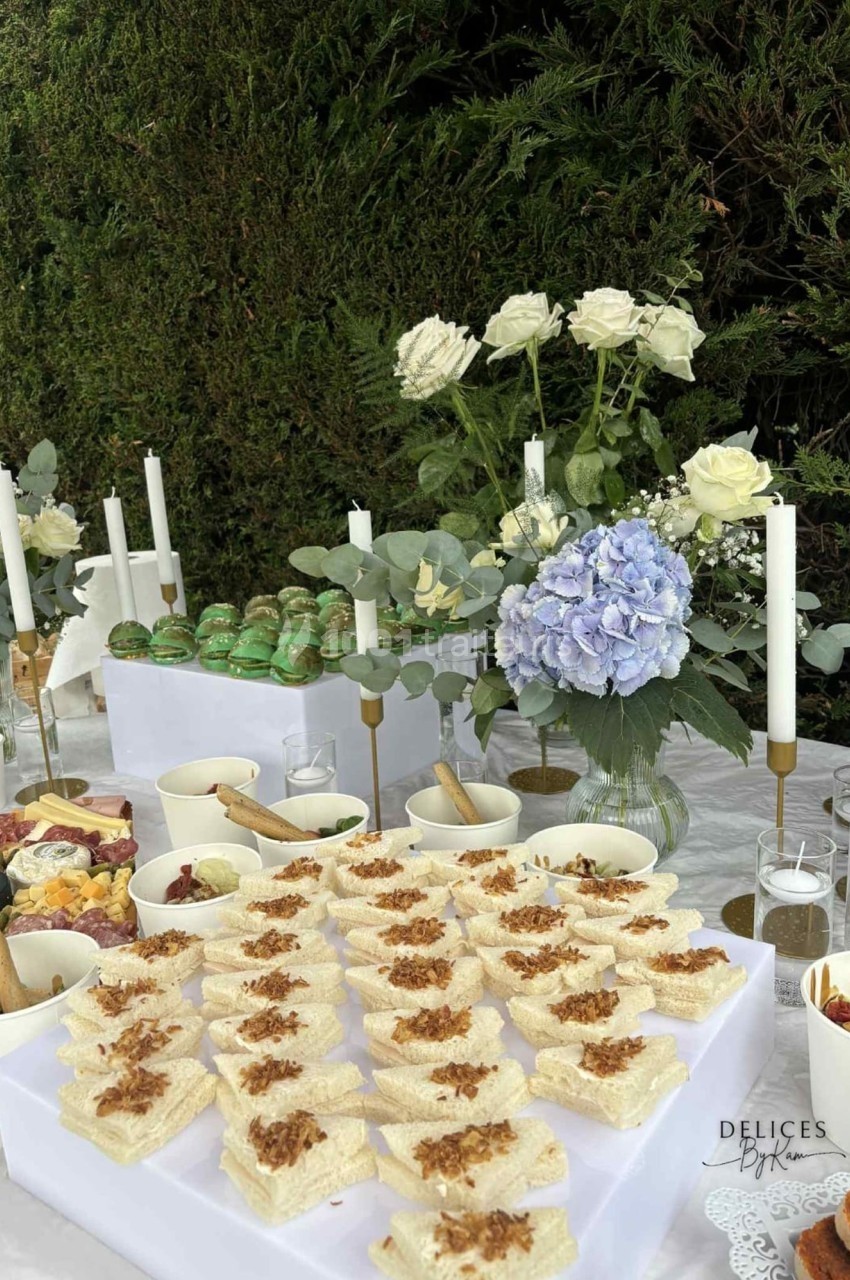 Table dressée en extérieur avec des fleurs, bougies et plats variés, incluant des amuse-bouches et des macarons.