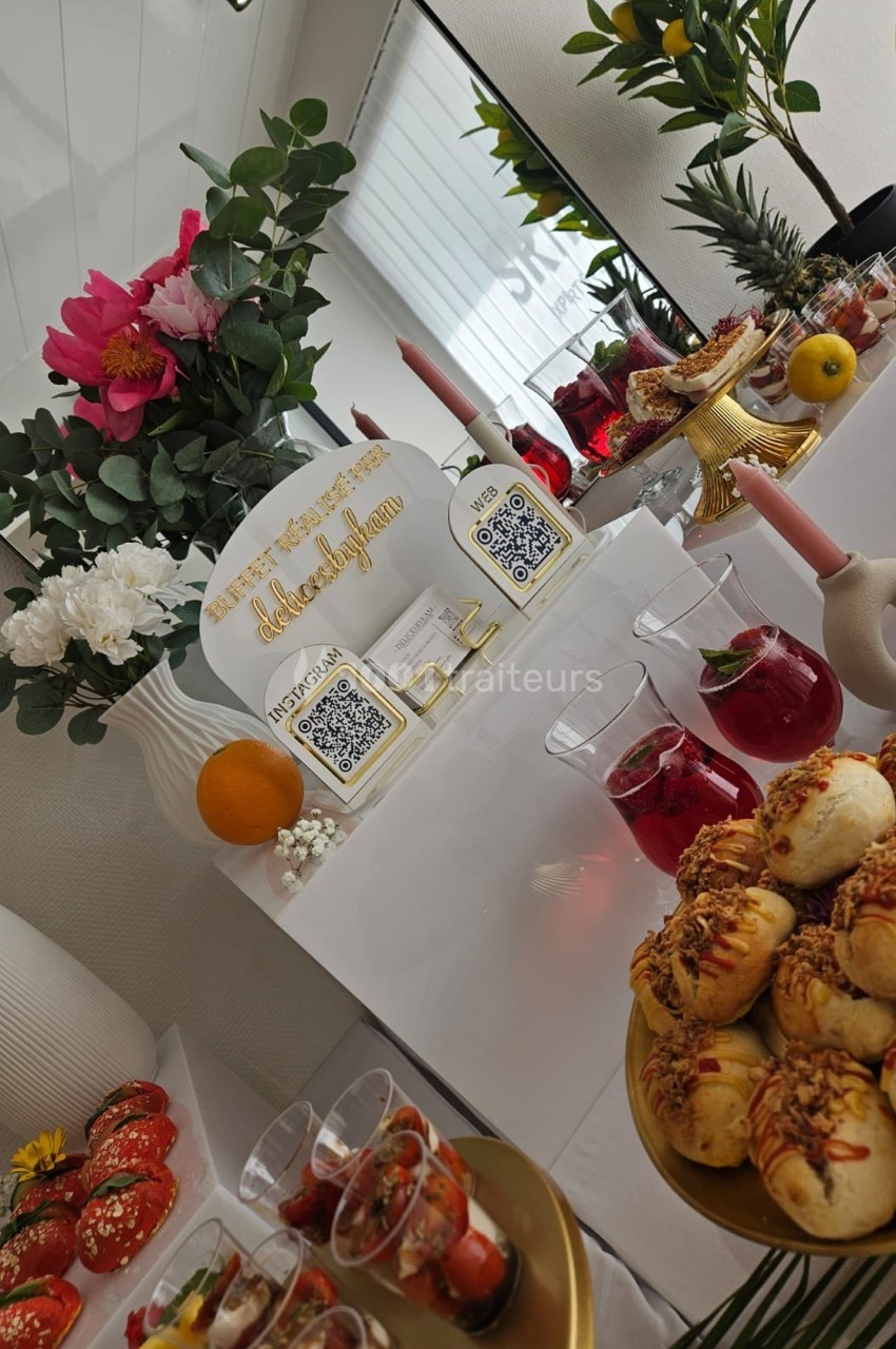 Table garnie de viennoiseries, boissons rouges, fleurs et éléments décoratifs dans un cadre élégant et lumineux.