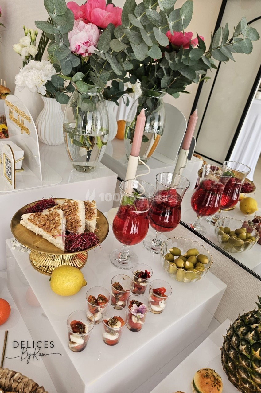 Table garnie de desserts, verrines, boissons rouges, olives, fruits et décorations florales dans un cadre élégant.