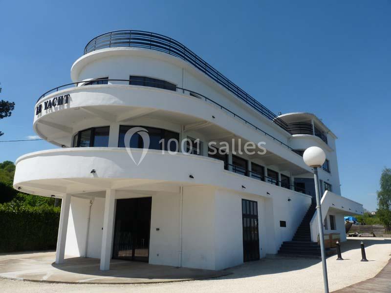Bâtiment blanc moderne en forme de paquebot avec balcons arrondis et inscription ’Le Yacht’ sur la façade.