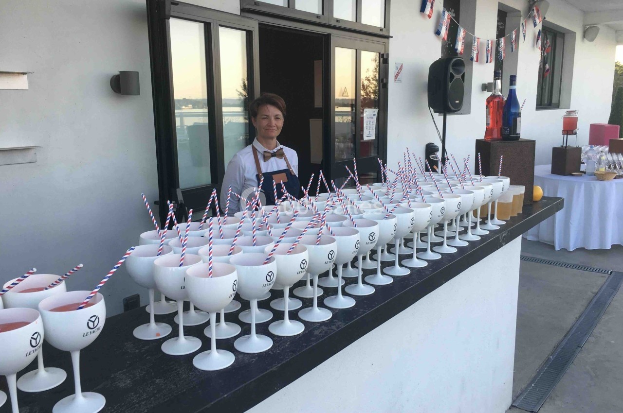 Serveur derrière un comptoir extérieur avec des verres blancs alignés, décorations festives en arrière-plan.