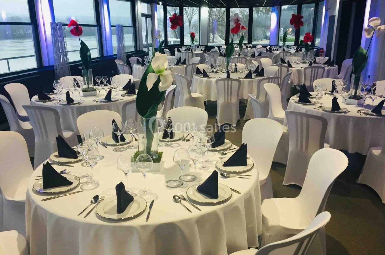Salle de réception élégamment décorée avec des tables rondes dressées, nappes blanches et centres de table fleuris.