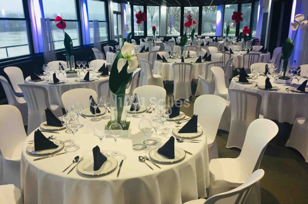 Salle de réception élégamment décorée avec des tables rondes dressées, nappes blanches et centres de table fleuris.