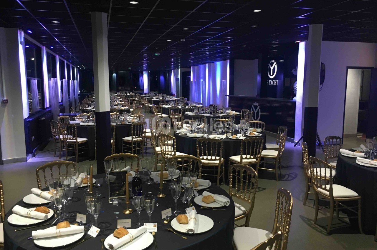 Salle de réception élégamment décorée avec tables rondes, nappes noires, chaises dorées et couverts dressés.