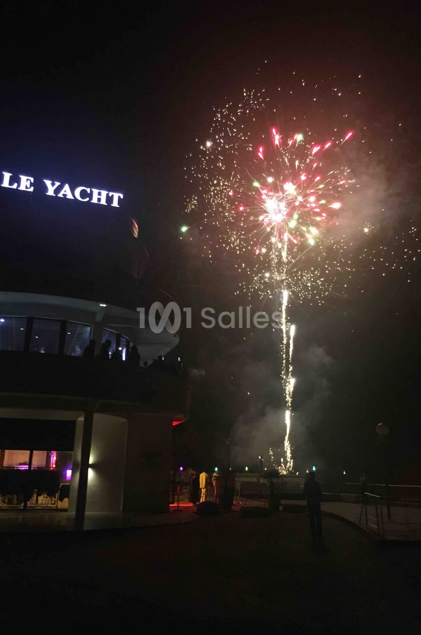 Feu d'artifice illuminant le ciel nocturne près d'un bâtiment avec l'enseigne ’Le Yacht’.