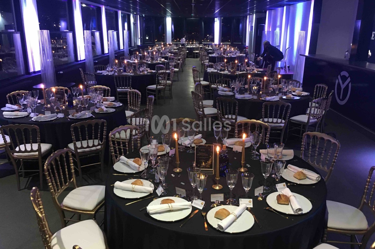 Salle de réception élégamment décorée avec des tables rondes, nappes noires, chandeliers et couverts dressés.