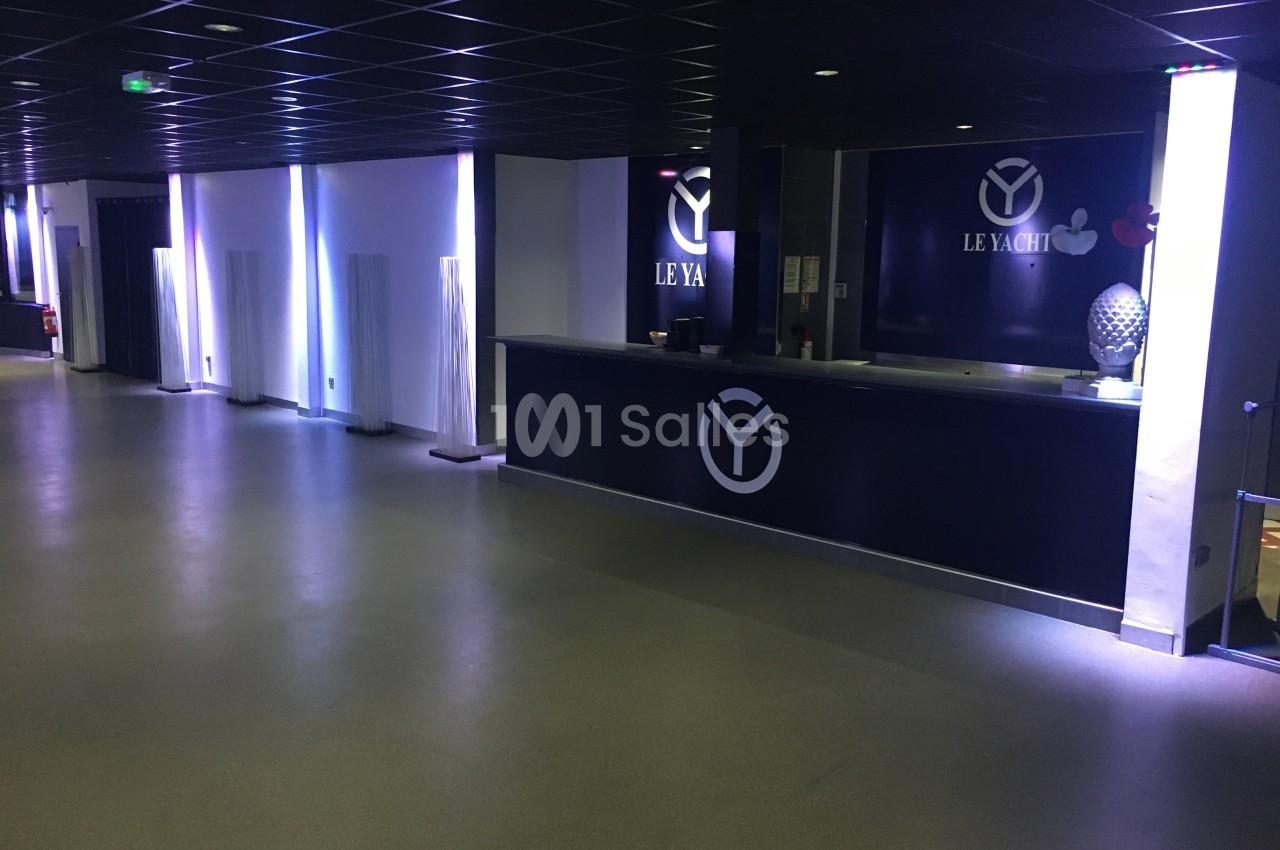 Vue d'un hall moderne avec un comptoir noir marqué ’Le Yacht’, éclairage tamisé et décor minimaliste.