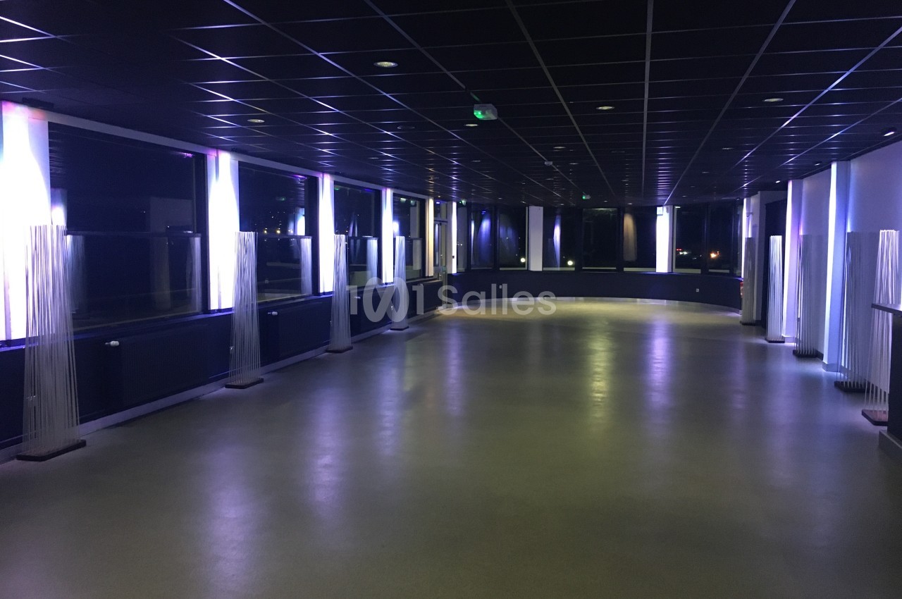 Salle vide avec sol clair, murs sombres et éclairage lumineux diffusé par des colonnes lumineuses modernes.