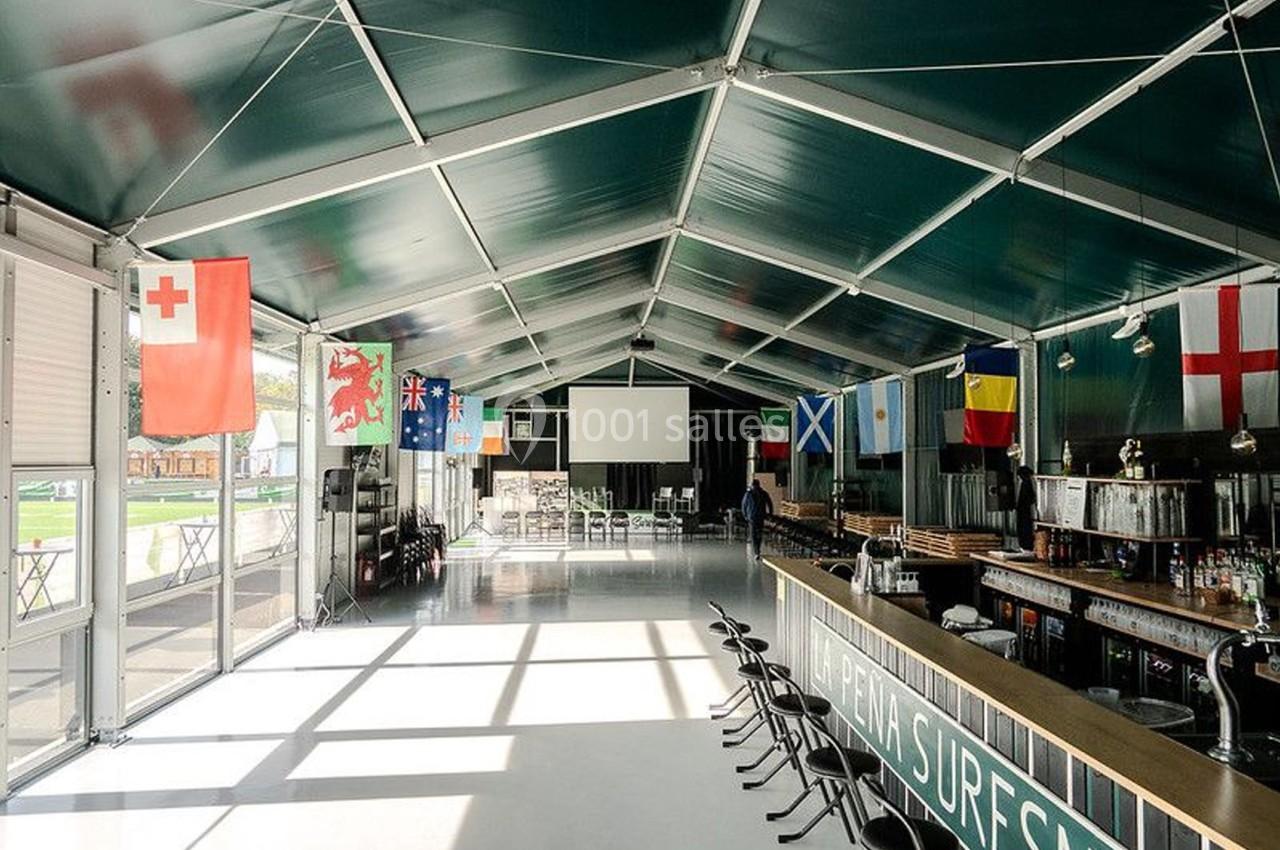 Intérieur d'une grande tente avec un bar, des drapeaux suspendus et des tables disposées au fond.