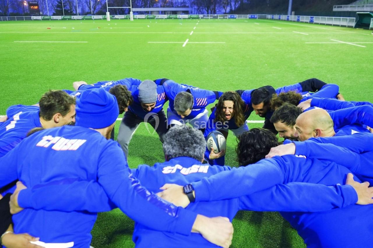 Des joueurs de rugby en cercle sur un terrain, se préparant avant un match en tenant un ballon.