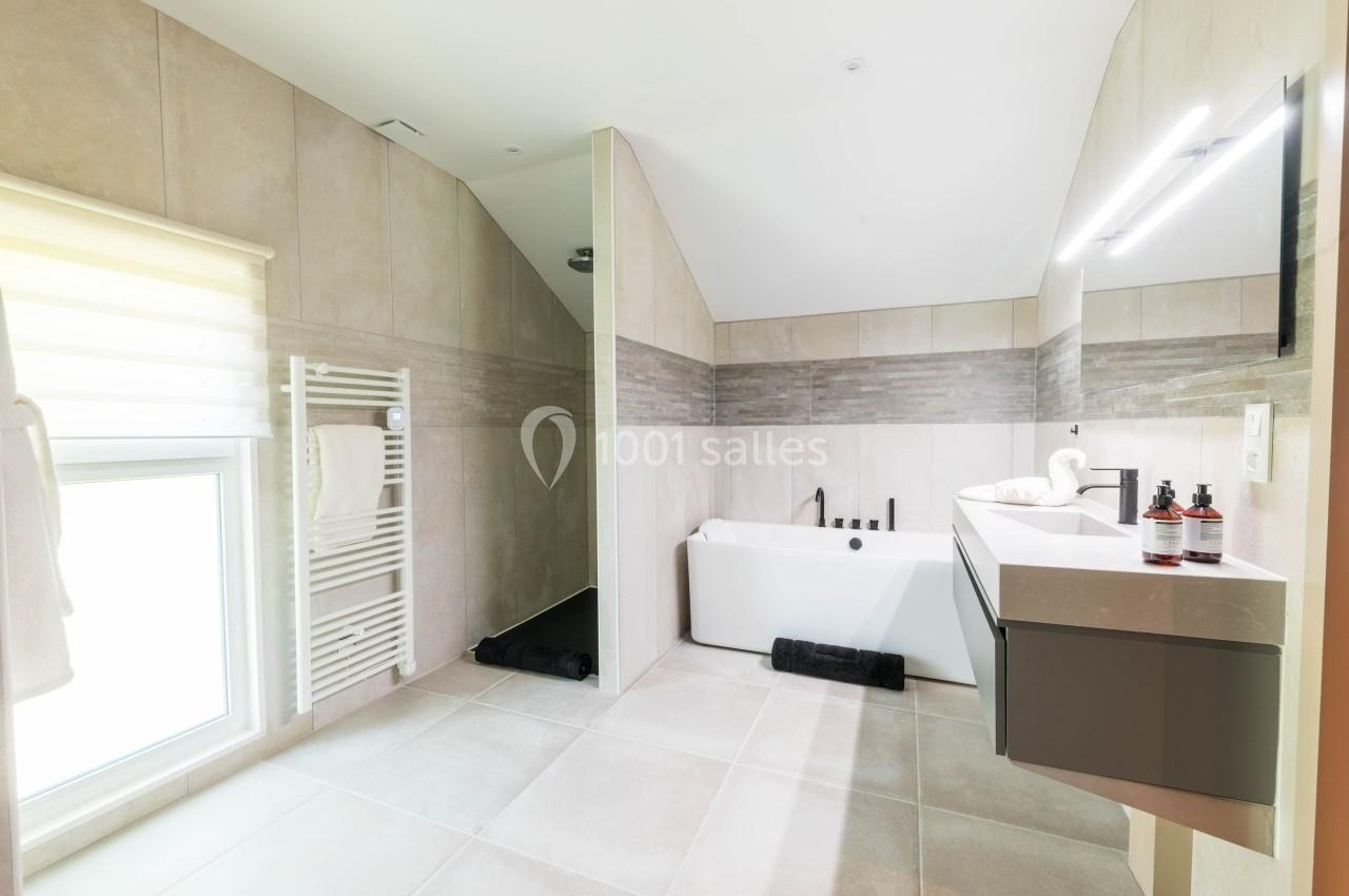 Salle de bain moderne avec baignoire, vasque suspendue, radiateur sèche-serviettes et lumière naturelle.