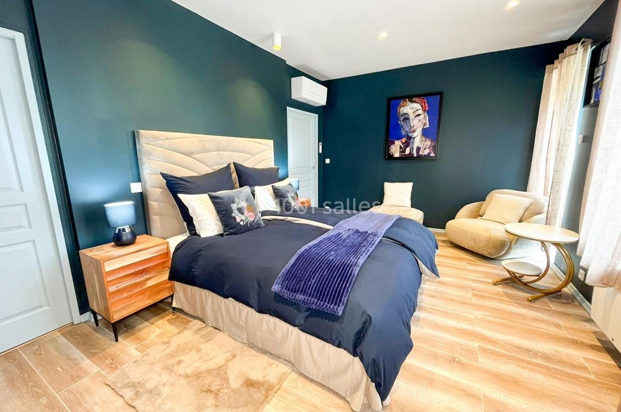 Chambre moderne avec murs bleu foncé, lit double, fauteuil beige, parquet clair et éclairage intégré.