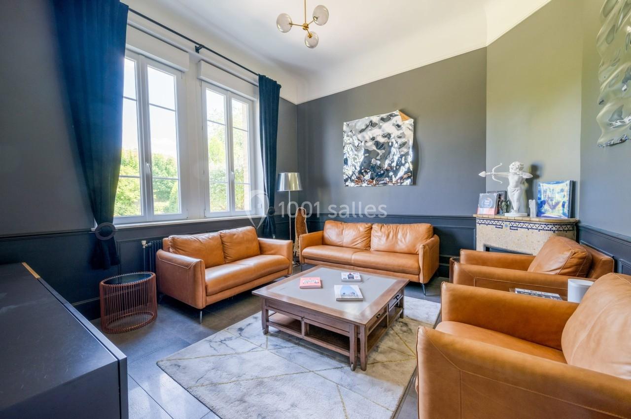 Salon lumineux avec murs sombres, mobilier en cuir marron, table basse en bois et grande fenêtre donnant sur un jardin.