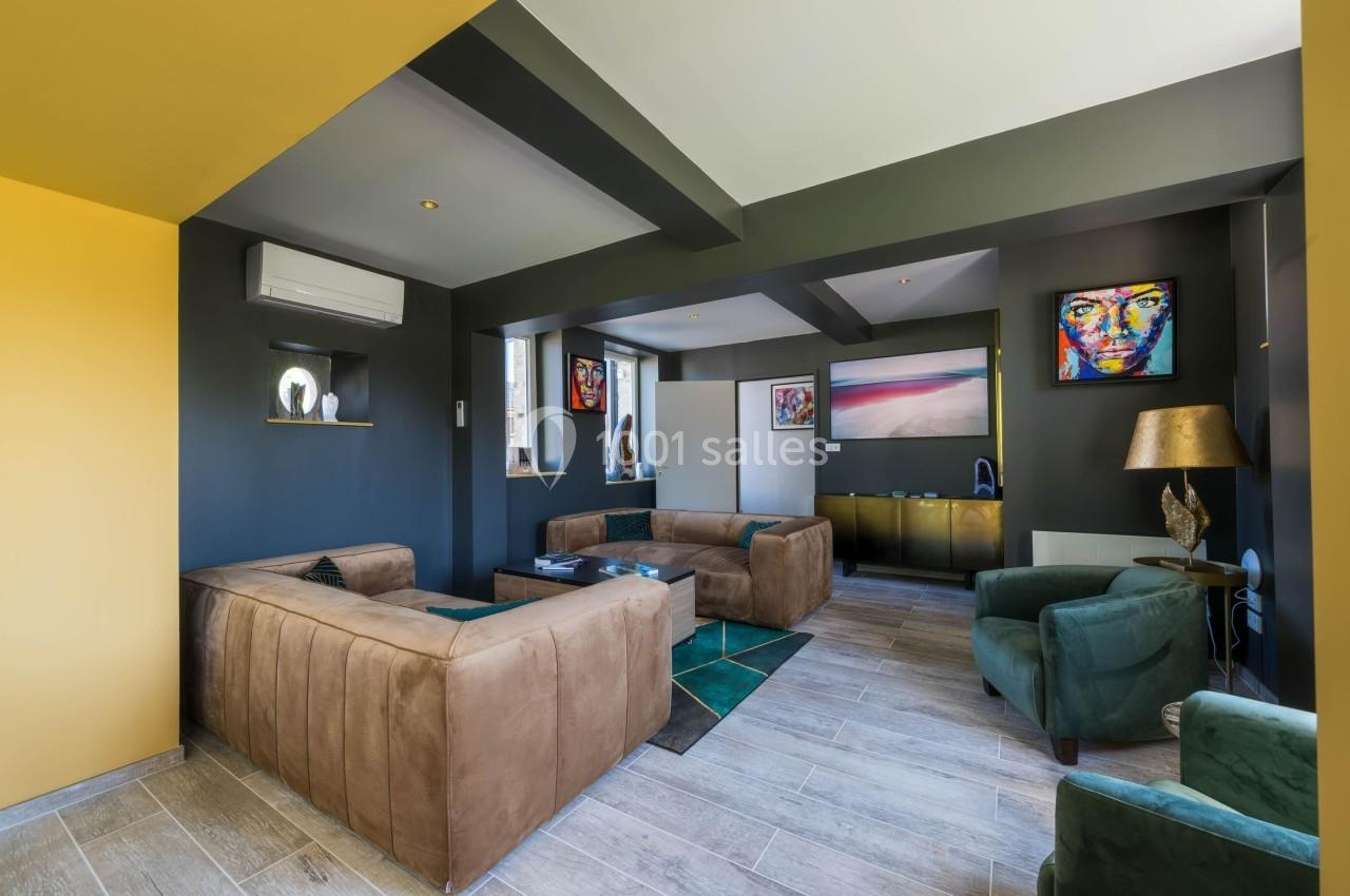 Salon moderne avec canapés en velours, murs sombres, œuvres d'art colorées et éclairage naturel.