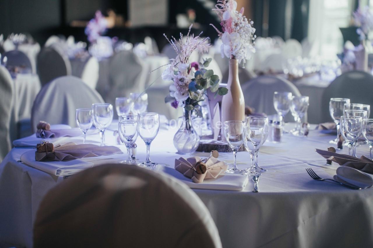 Table décorée avec nappes blanches, verres, serviettes pliées et arrangements floraux dans une salle de réception.