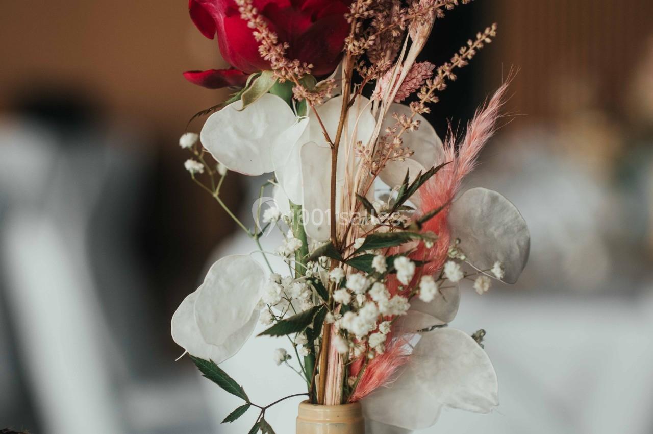 Composition florale dans un vase beige, avec une rose rouge, des fleurs blanches et des herbes séchées.