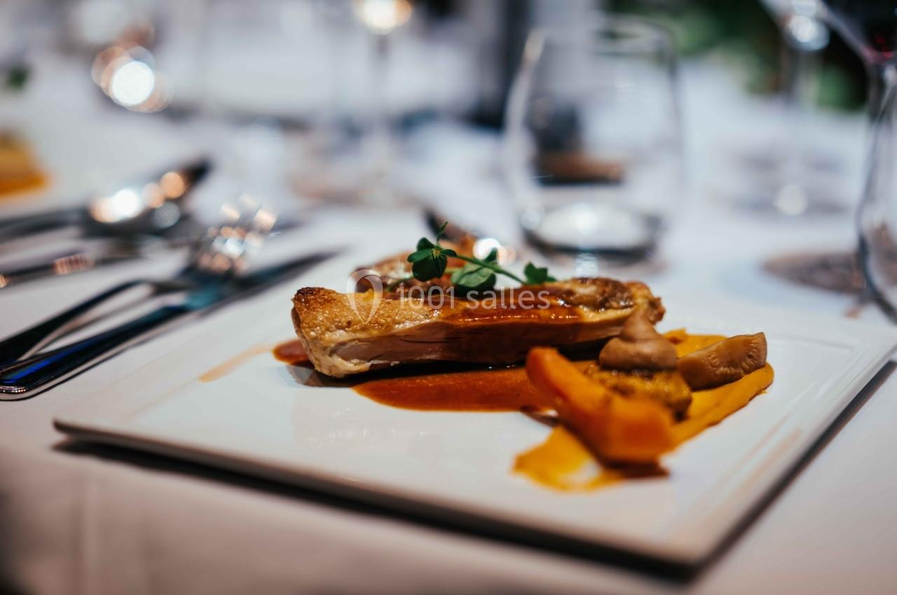 Plat de viande grillée accompagné de légumes et sauce, servi sur une assiette blanche dans un cadre de table élégamment…