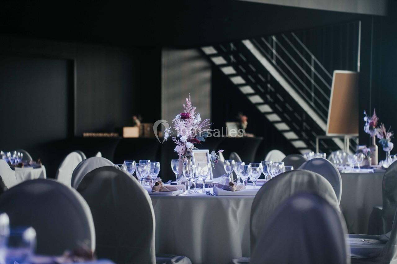 Salle de réception élégante avec tables dressées, nappes blanches et décorations florales au centre.