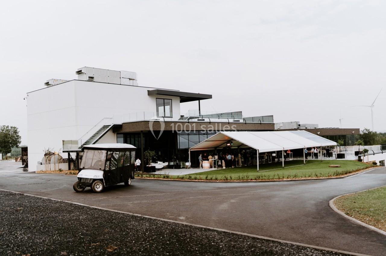 Bâtiment moderne avec une tente blanche installée sur une pelouse, et une voiturette de golf stationnée au premier plan.