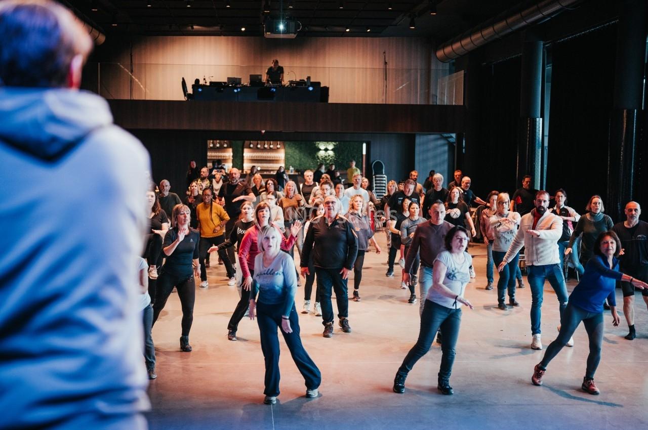Groupe de personnes dans une salle, participant à une activité collective dirigée par un animateur.