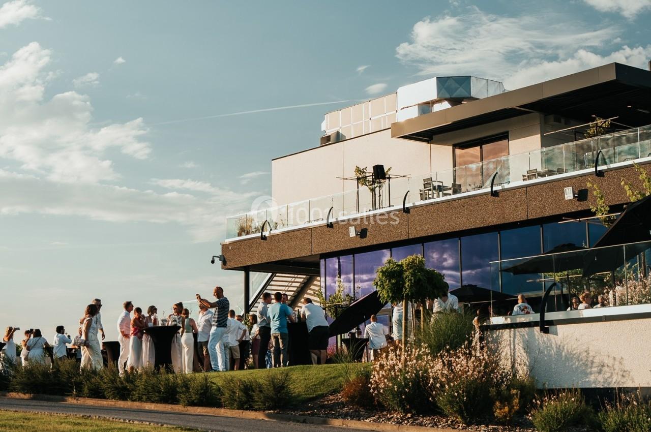 Groupe de personnes rassemblées sur une terrasse extérieure moderne lors d'un événement par une journée ensoleillée.