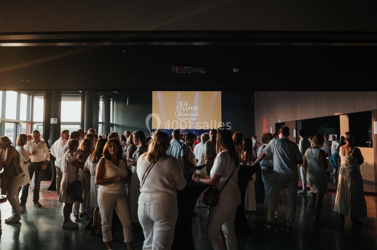 Groupe de personnes en tenue blanche rassemblées dans une salle sombre avec un écran lumineux en arrière-plan.